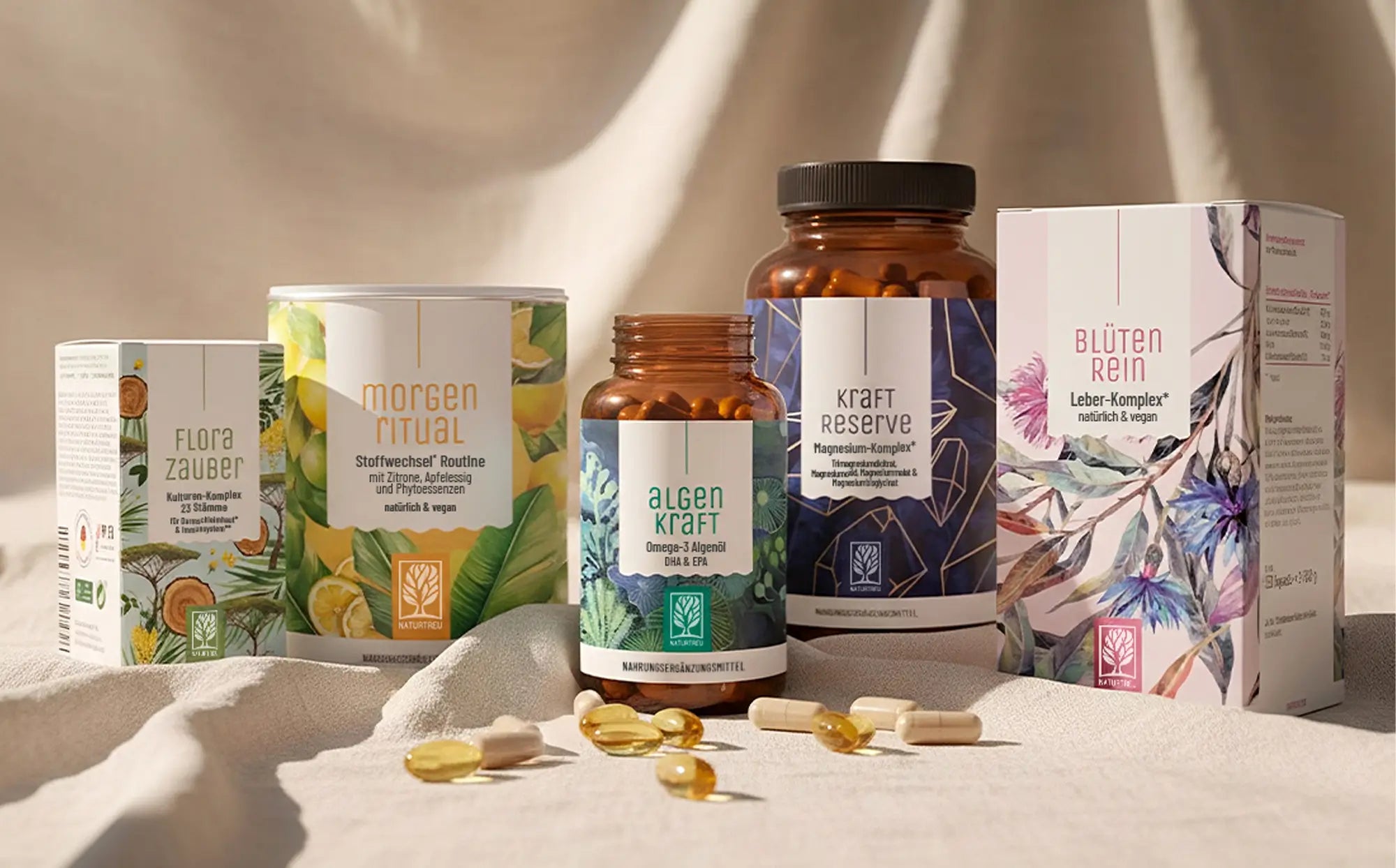 Eine Sammlung von beliebten NATURTREU-Produkten auf einem weißen Tuch in warmen Licht. Produkte von links nach rechts: Florazauber, Morgenritual, Algenkraft, Kraftreserve, Blütenrein.